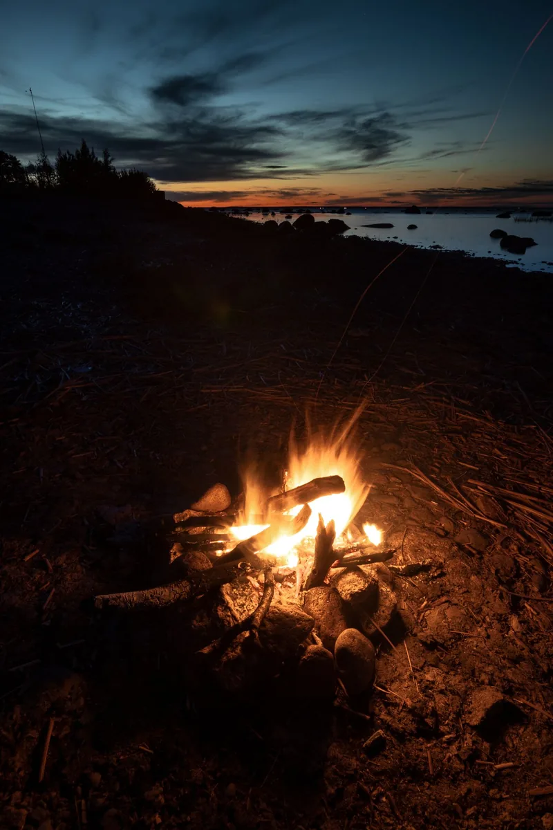 A tranquil beach campfire glowing at sunset, offering warmth and serenity