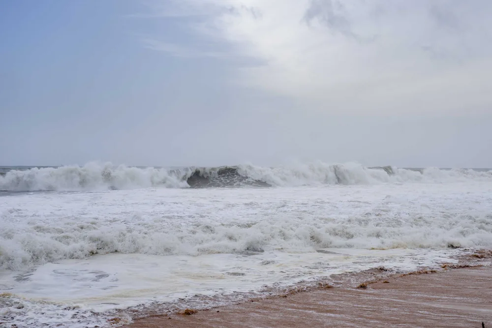 Dramatic ocean waves crashing on the sandy shore with a cloudy sky backdrop