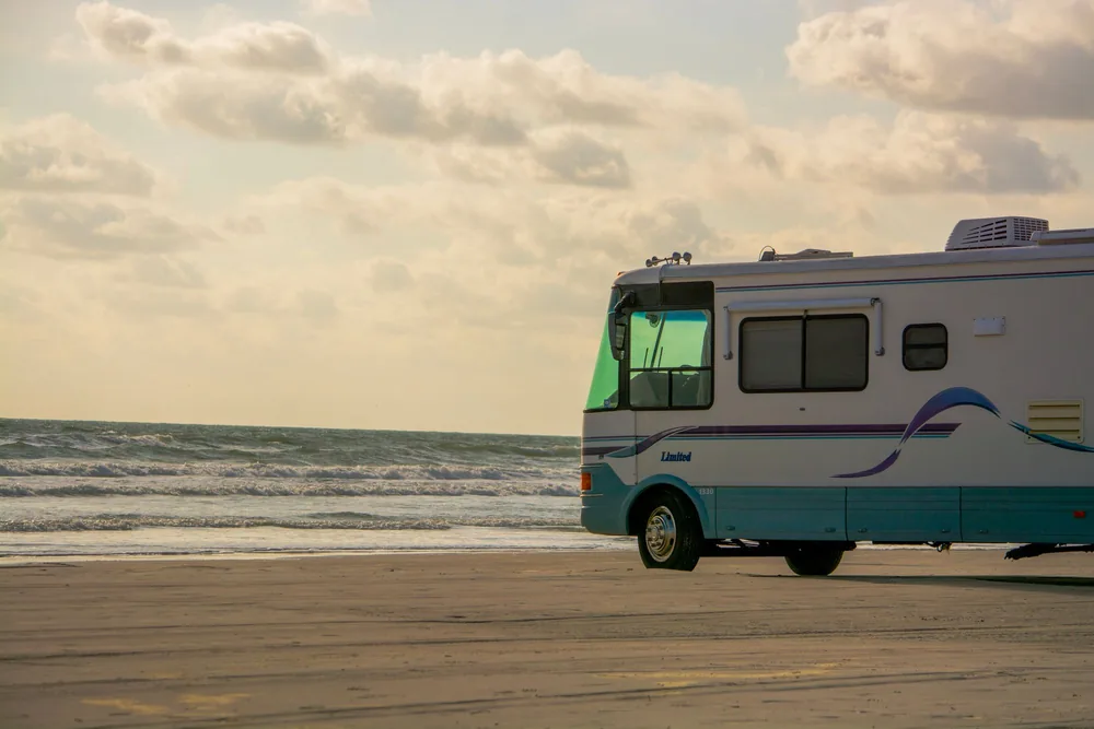 An RV parked on a sandy beach with the ocean and cloudy sky in the background