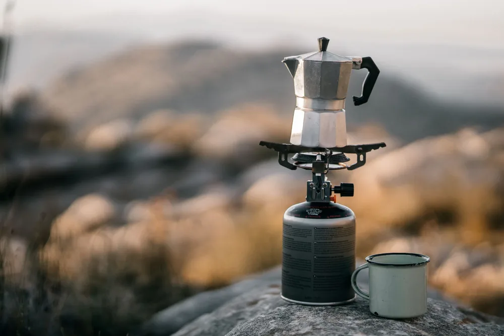 A close-up of a coffee pot on a camping stove outdoors, evoking an adventure vibe