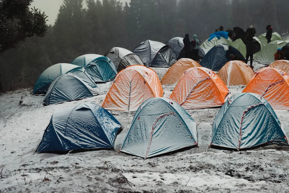 A vibrant campsite with colorful tents in a snowy forest in Singtur Range, India, capturing the essence of winter camping
