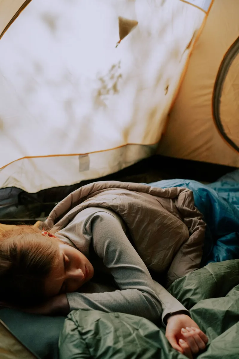 A woman peacefully sleeping in a tent, surrounded by a cozy sleeping bag and nature