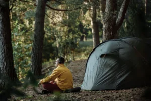 A person enjoying a calm morning by a tent in a forest wearing headphones