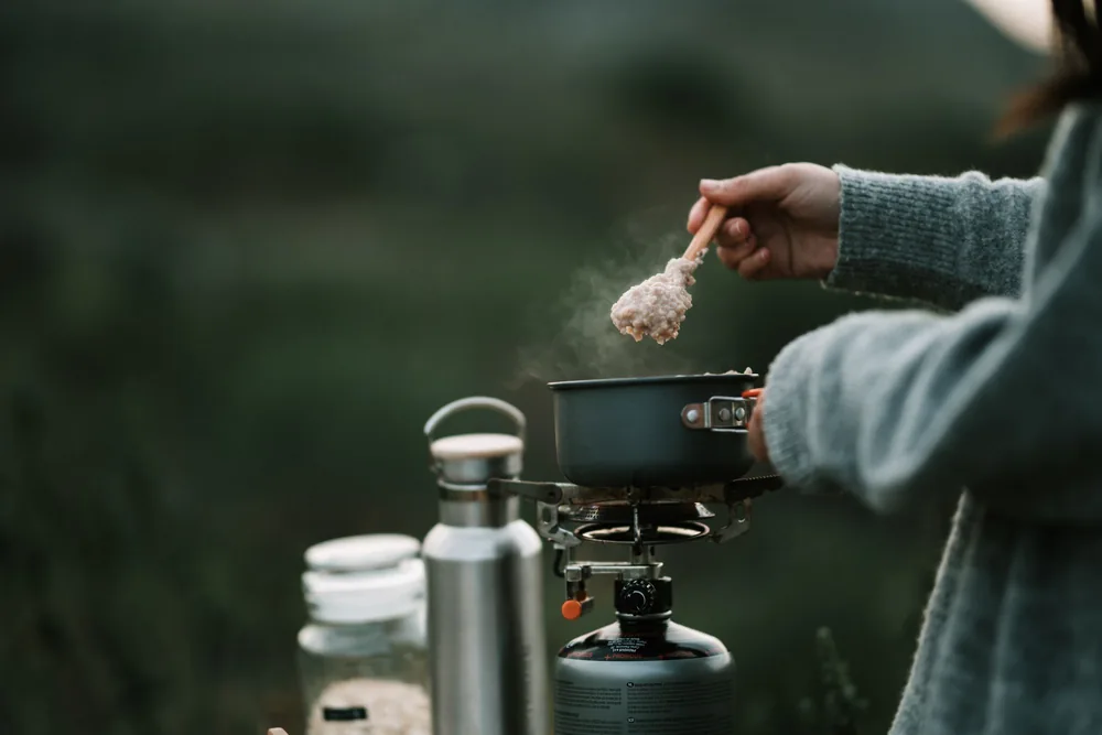 A person is cooking steaming oatmeal on a portable stove during a camping trip