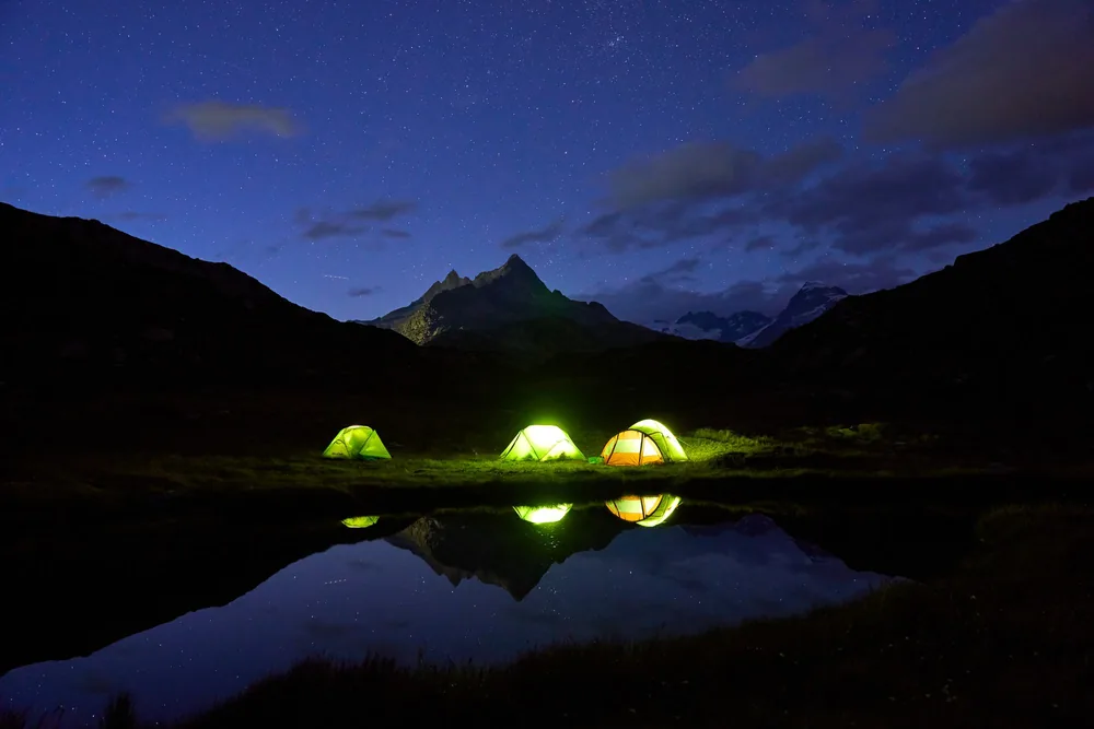 A tranquil night camping by a mountain lake with glowing tents under a starlit sky